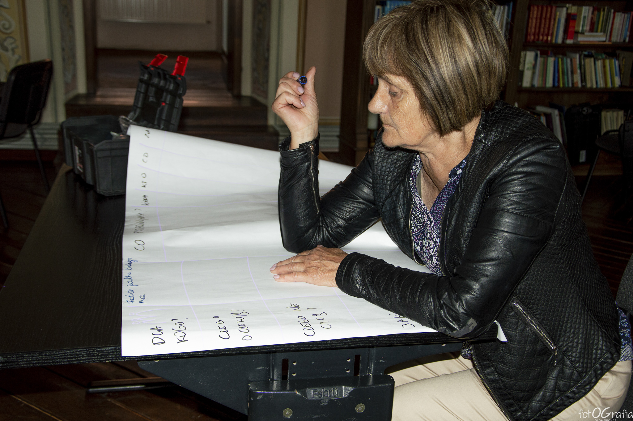 Zdjęcie przedstawia kobietę piszącą na dużej kartce papieru.